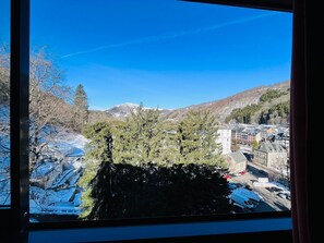 Une vue à travers une fenêtre, avec une montagne en arrière-plan, des arbres et un bâtiment dont le sol est recouvert de neige.