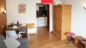 Un soggiorno accogliente con un divano grigio, un tavolo da pranzo in legno con sedie, una cucina sullo sfondo e un armadio in legno.