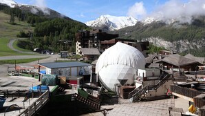 Un edificio con una grande struttura a cupola, immerso in un paesaggio montuoso e sotto un cielo sereno.