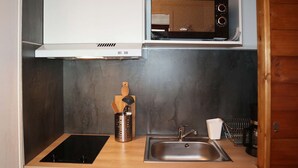 Una cucina compatta con forno a microonde, lavello, piccolo frigorifero e tagliere in legno con utensili.