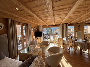 Een houten interieur met een bank, stoelen, een eettafel en een televisie.