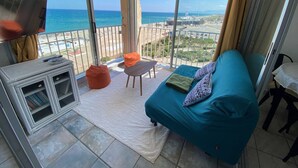 A balcony with a sofa, a small table, and a TV. - Large Studio for 2, Sea View, Private Parking (Le Barcarès)