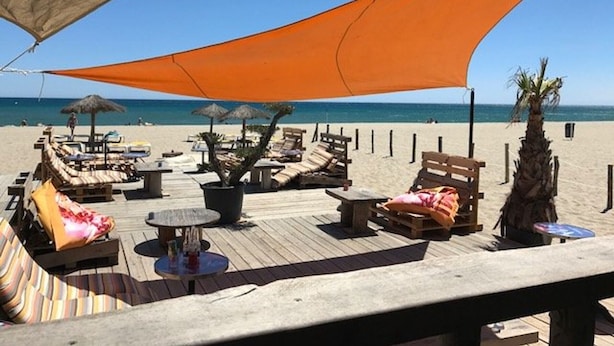 A beachside lounge area with wooden lounge chairs, umbrellas, and a wooden deck. - Large Studio for 2, Sea View, Private Parking (Le Barcarès)
