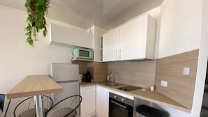A compact kitchen with a refrigerator, microwave, sink, and stove. There is a small dining area with a table and two chairs. - Large Studio for 2, Sea View, Private Parking (Le Barcarès)