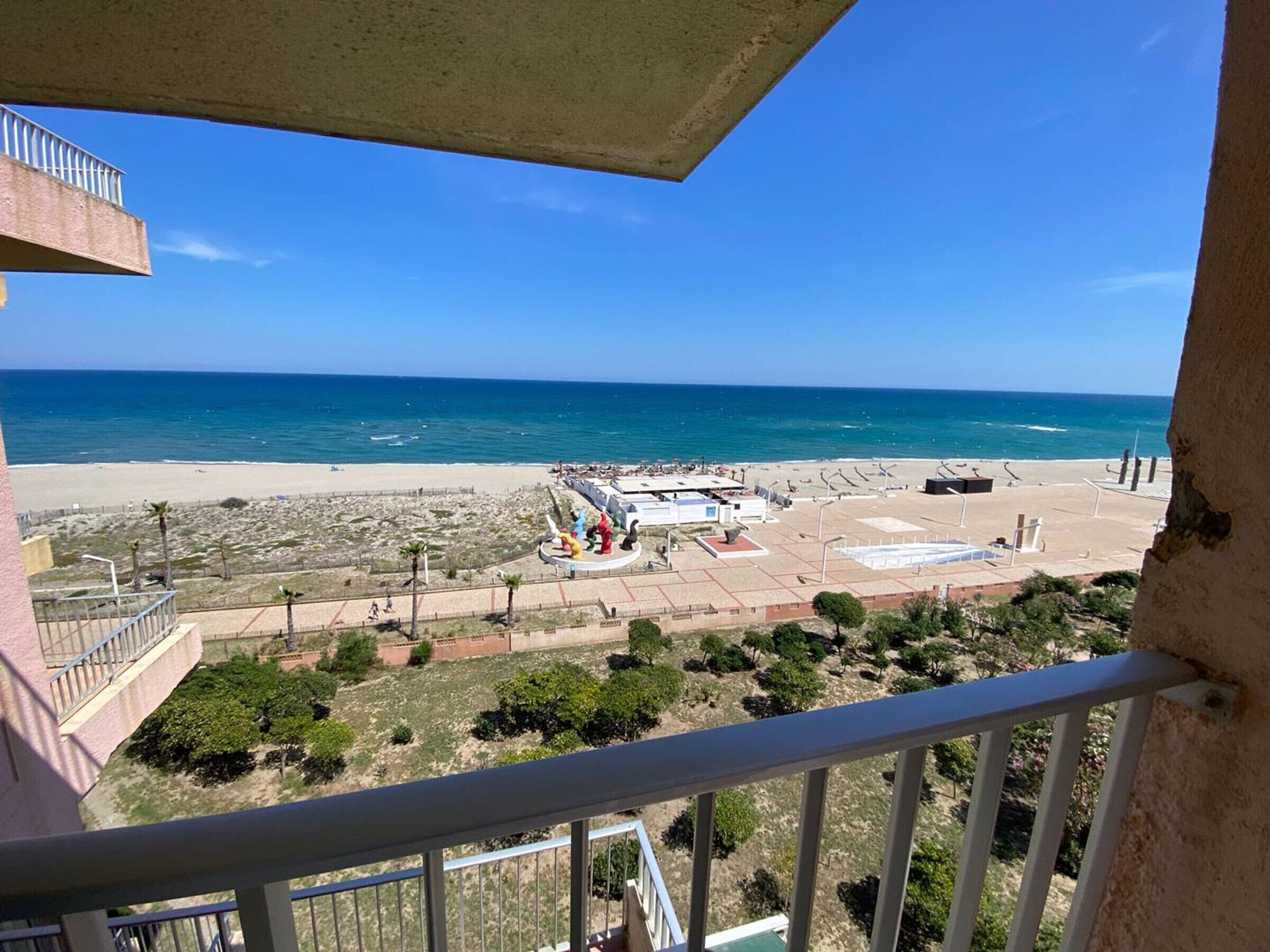 A balcony with a view of a beach and a sculpture garden.