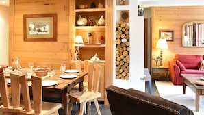 Een houten interieur met een eethoek, een open haard, planken met decoratieve objecten en een gezellige zithoek.