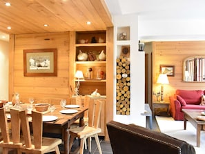 A wooden interior with a dining area, a fireplace, shelves with decorative items, and a cozy seating area.
