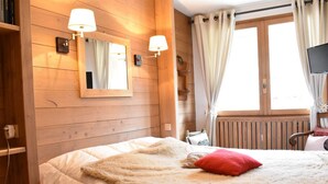 Een knus slaapkamer met houten wanden, een groot bed met zachte beddengoed, een rode kussen en twee wandlampen.