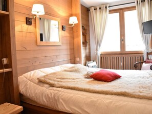 A cozy bedroom with wooden walls, a large bed with fluffy bedding, a red pillow, and two wall-mounted lamps.