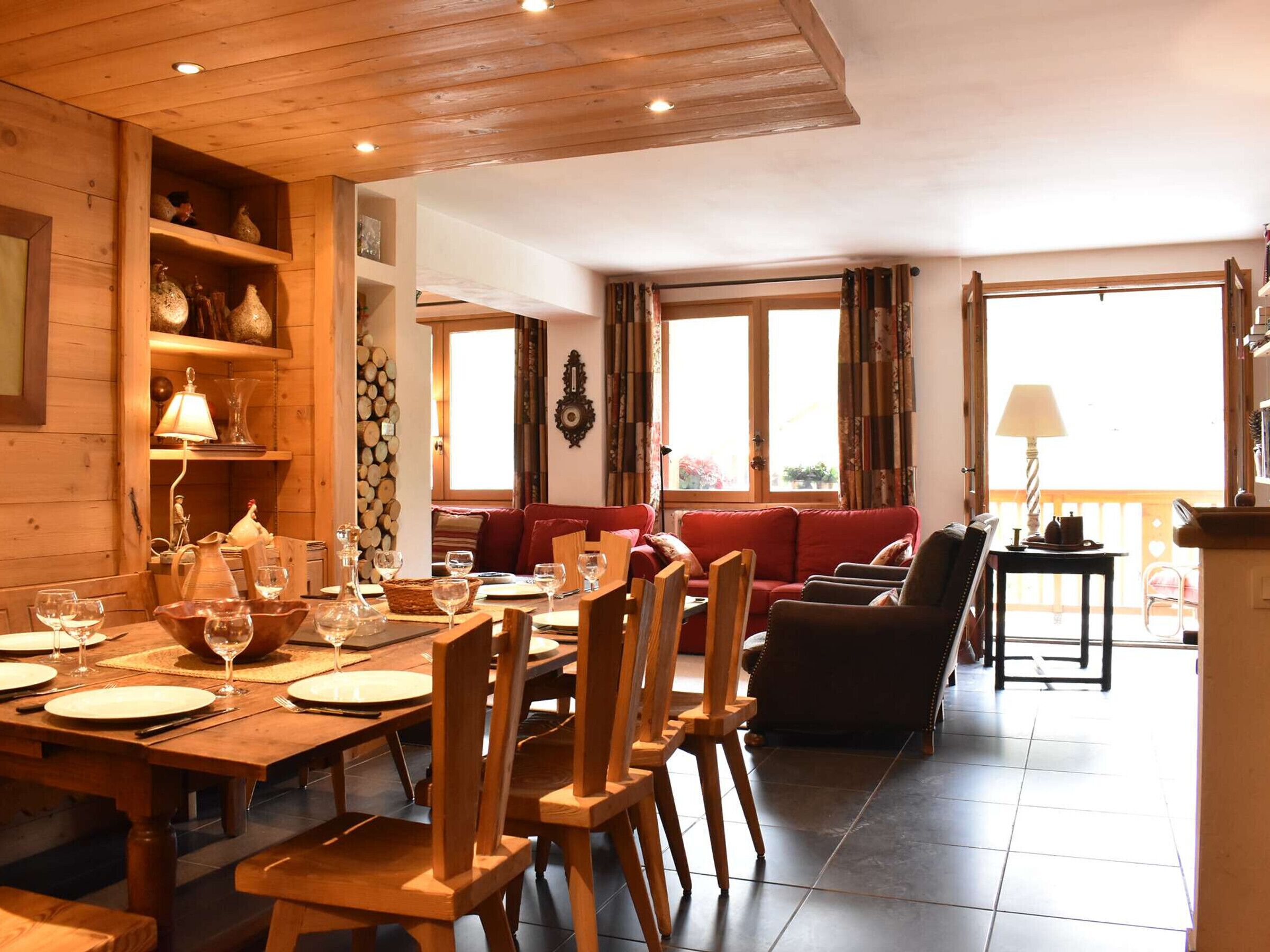 Ein Holzkaminzimmer mit Esstisch für vier Personen, einem roten Sofa und einem kleinen Tisch mit Lampe.