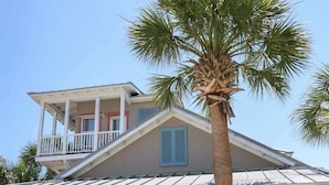 Una casa a due piani con un balcone, un portico e diverse palme nel giardino.