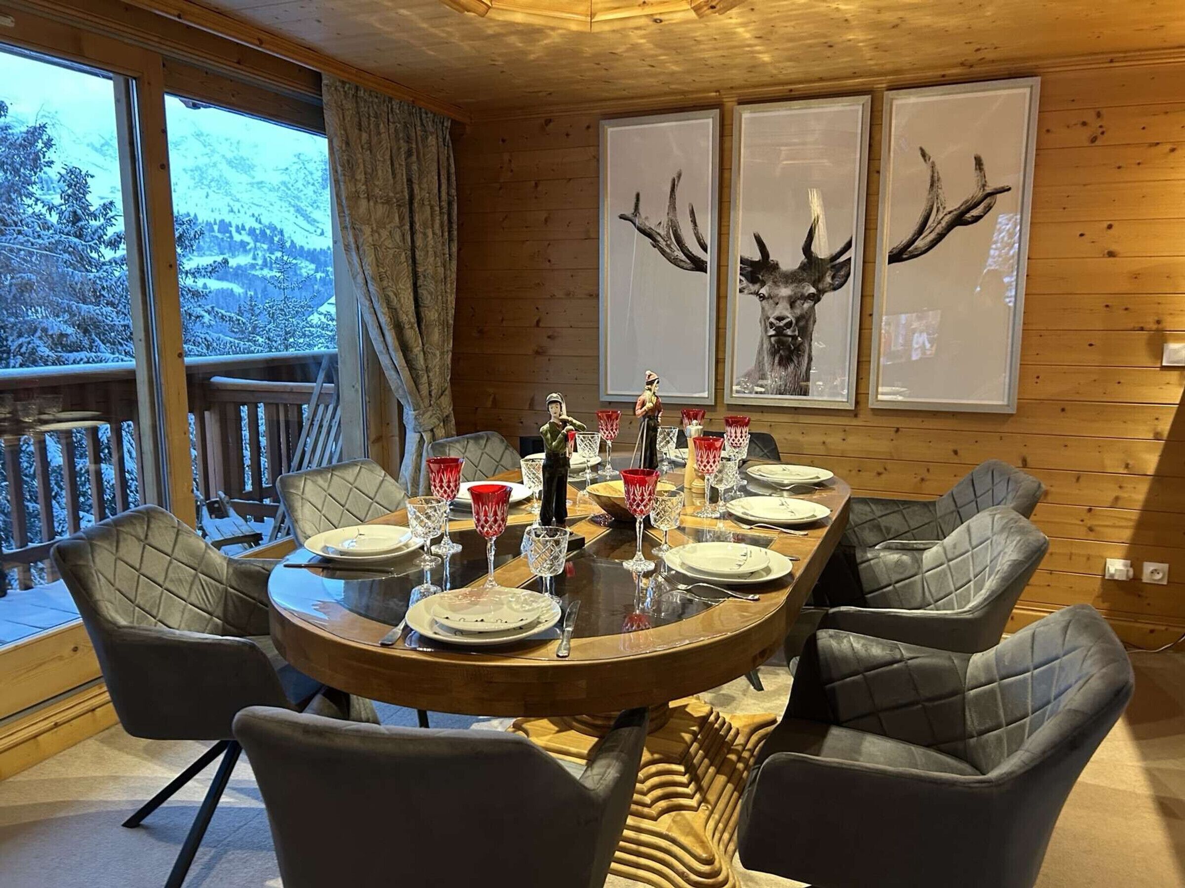 A dining area with a wooden table set for six, surrounded by leather chairs. There are framed pictures of deer antlers on the wall.