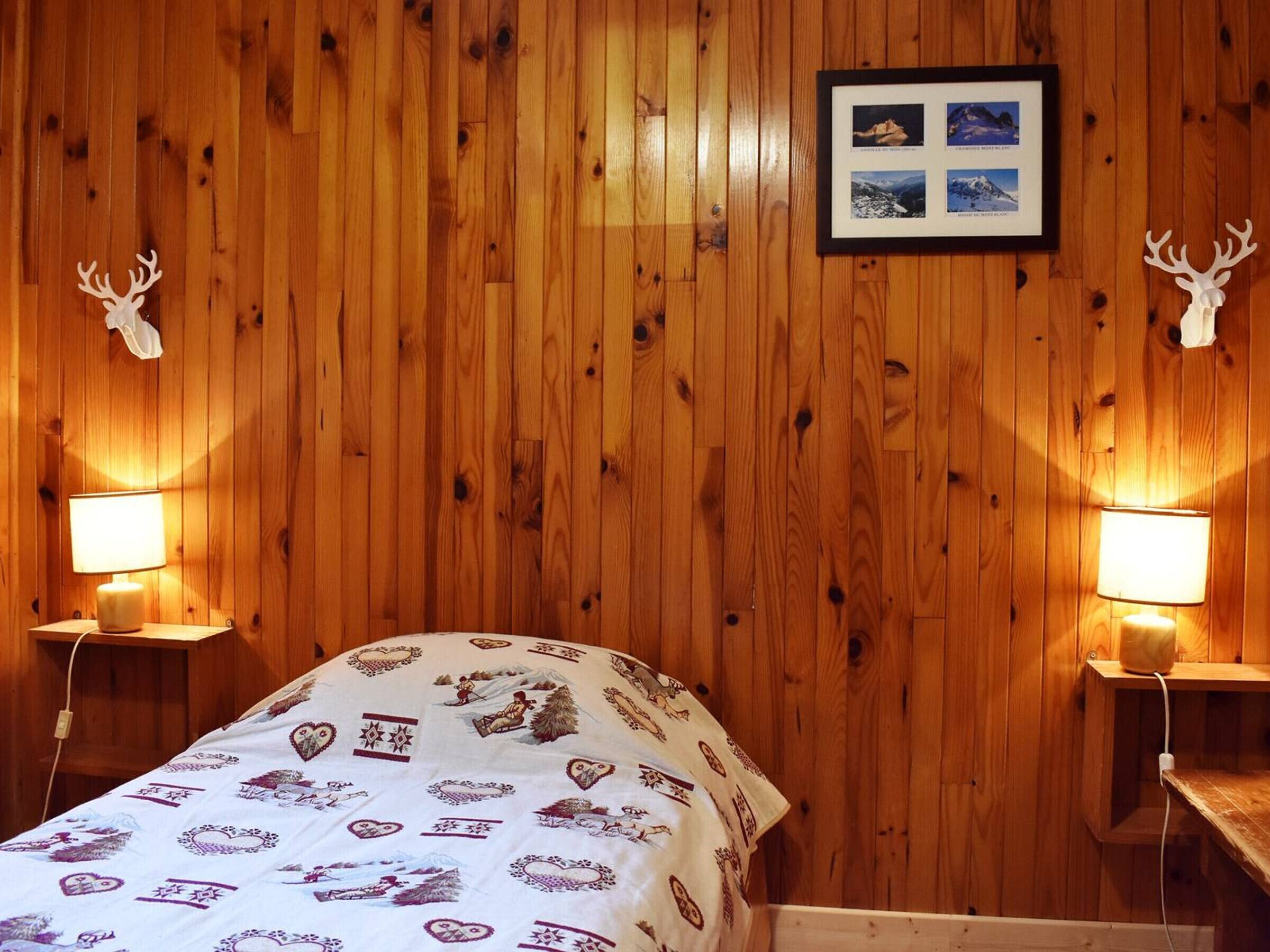 A wooden-paneled room with a bed, two bedside lamps, and a framed picture on the wall.