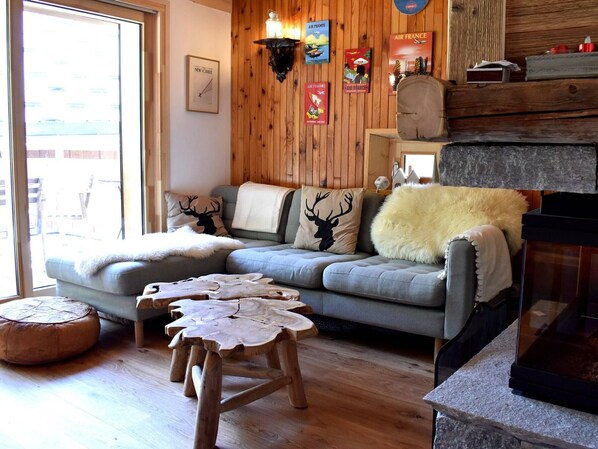 Ein gemütliches Wohnzimmer mit grauem Sofa, Holzelementen und einem Kamin.