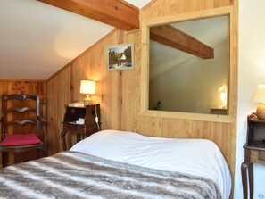 Ein gemütliches Zimmer mit einem Bett, einem Holzstuhl, einem Schreibtisch mit Lampe und einem Bild an der Wand.