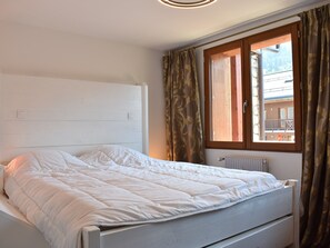 Un lit simple avec une tête de lit et un pied de lit blancs, une fenêtre avec des rideaux et un radiateur.