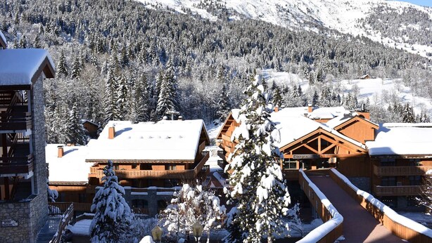 Ein mit Schnee bedecktes Chalet mit Holzbalkon, einer Seilbahn und einem Berg im Hintergrund.