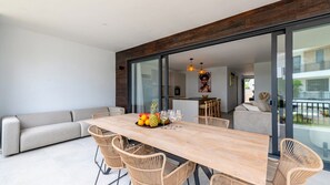 A modern living space with a dining area, a sofa, and a kitchen visible through glass doors.