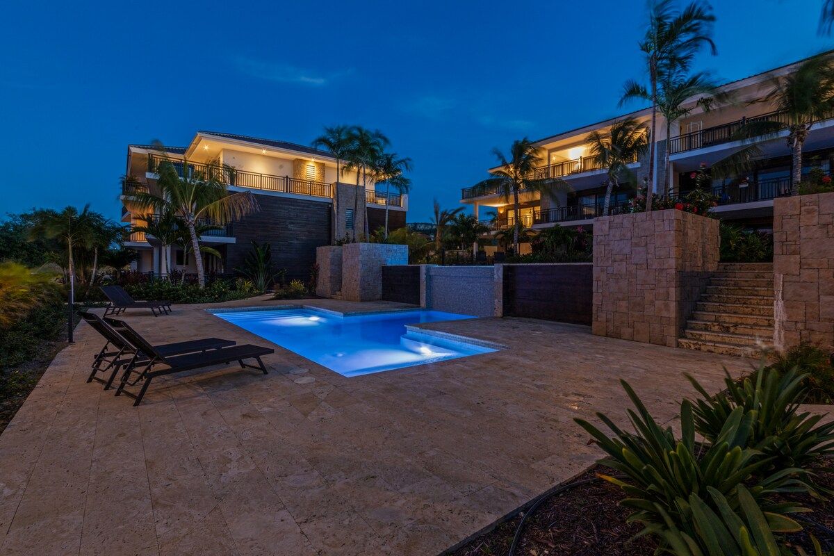 A modern hotel with a swimming pool, lounge chairs, and a well-maintained garden.
