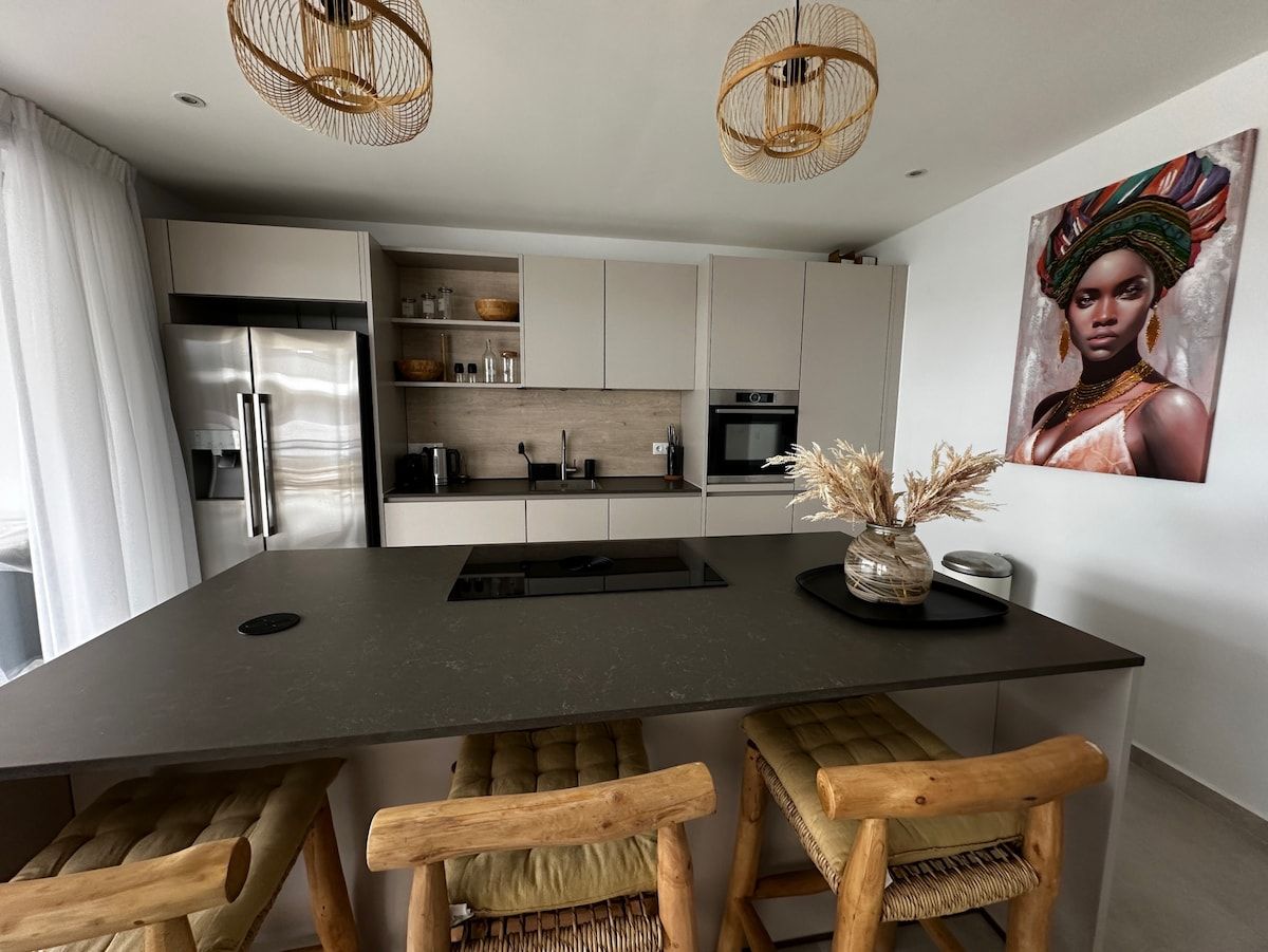 A modern kitchen with a central island, wooden chairs, and a dining table.