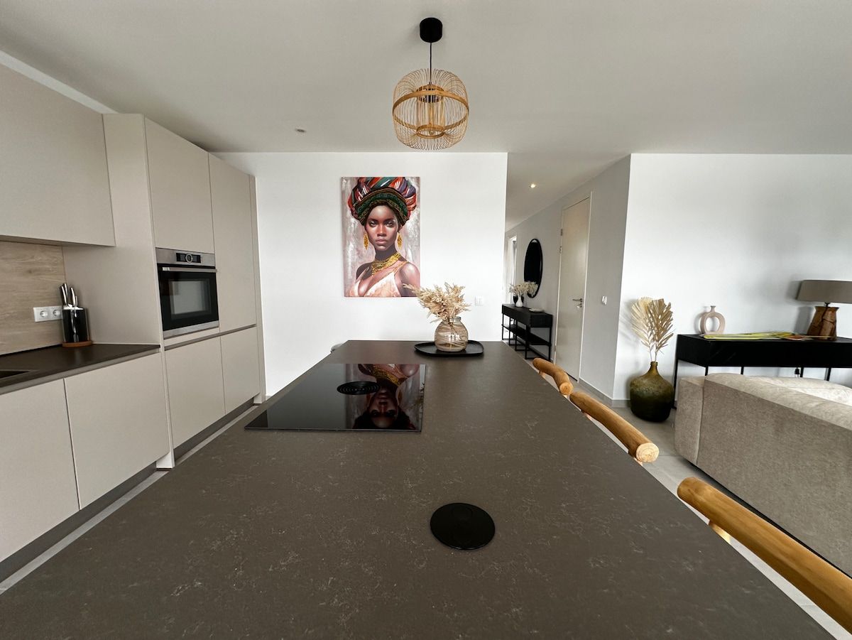 A modern kitchen with a central island, built-in oven, and a hanging light fixture.