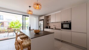 A modern kitchen with a large island, stainless steel appliances, and wicker chairs.