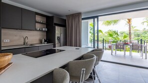 A modern kitchen with a central island, bar seating, and a view of a tropical landscape.