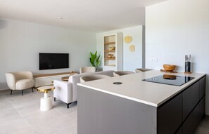 A modern kitchen with a central island, a flat-screen TV mounted on the wall, and a seating area with a sofa and chairs.