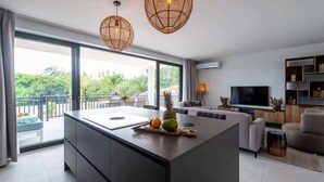 A modern kitchen with a large island, a dining area with a sofa, and a TV on the wall.