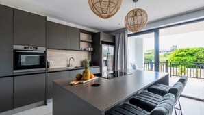 A modern kitchen with a central island, stainless steel appliances, and a view of greenery outside.