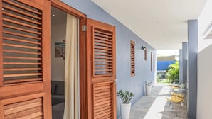 Un pasillo con puertas y contraventanas de madera, una planta en maceta y un espacio de descanso con sillas y una mesa.