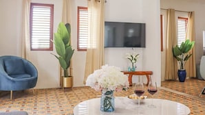 Una sala de estar moderna con un sillón azul, una mesa redonda de centro con un florero y un televisor de pantalla plana montado en la pared.