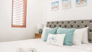 Una cama bien hecha con toallas enrolladas, un cabecero capitonado y una pared con cuadros enmarcados.