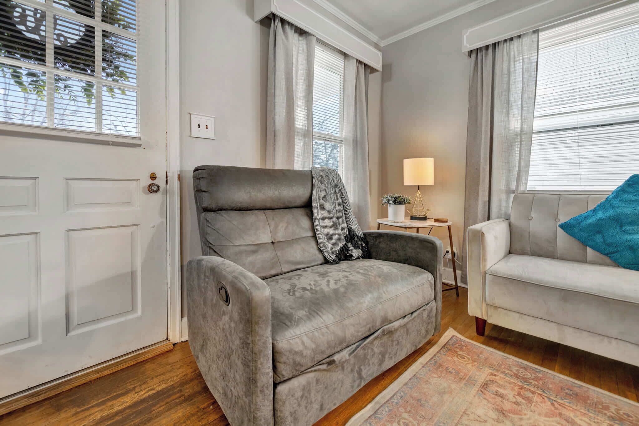 A living room with a grey sofa, a white sofa, a small table with a lamp, and a patterned rug.