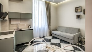 Een moderne keuken met een ingebouwde oven, een eethoek met een marmeren tafel, en een grijze bank in een zithoek.