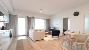 Una sala de estar moderna con sofá, mesa de comedor con sillas, televisor y área de cocina con armarios y cafetera.