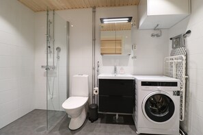 A modern bathroom with a glass shower enclosure, a toilet, a washing machine, and a sink. - Forenom Serviced Apts Espoo Matinkylä (Espoo)