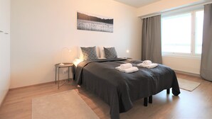 Un dormitorio moderno con una cama grande, una mesita de noche con lámpara, un cuadro en la pared y una ventana con cortinas.