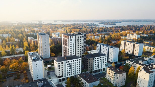 Complejo de edificios residenciales de gran altura con varios edificios de apartamentos, rodeado de árboles de colores otoñales y una masa de agua al fondo.