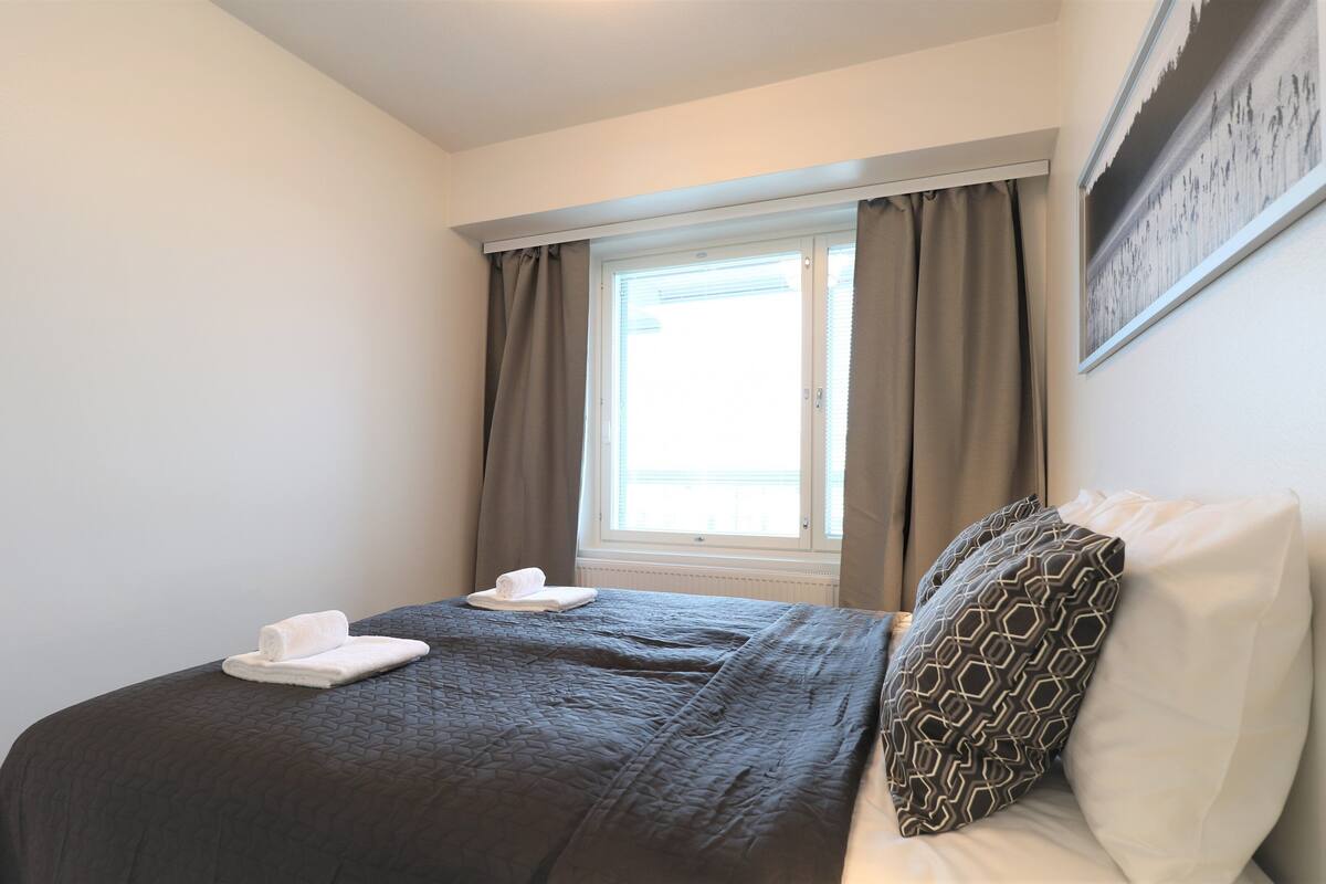 A bedroom with a bed, a window with curtains, and a framed picture on the wall.