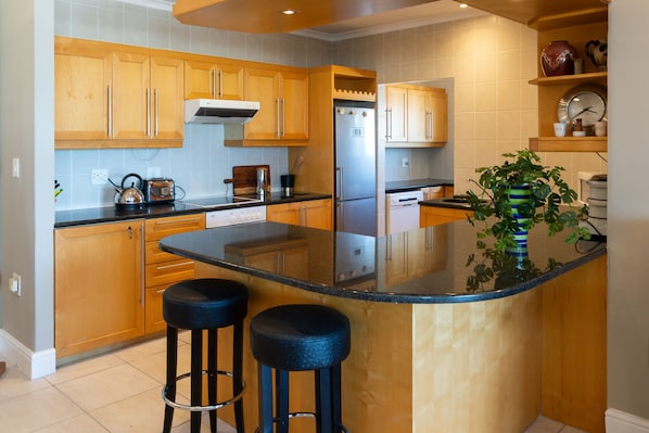 Cozinha moderna com armários de madeira, geladeira de aço inoxidável e uma ilha central com banquetas.