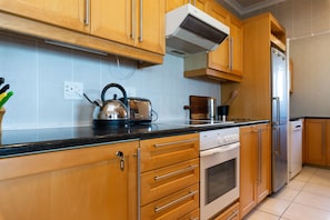 A kitchen with wooden cabinets, a stainless steel refrigerator, a dishwasher, and a stove. - Lagoon Beach Penthouse (Cape Town)