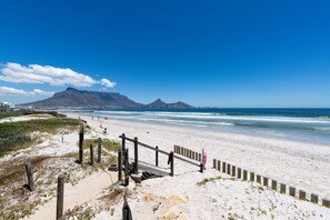 A beach with a wooden fence, sandy dunes, and a mountain in the background. - Lagoon Beach Penthouse (Cape Town)