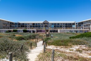 A modern hotel with a central courtyard, multiple balconies, and a sandy pathway leading to the entrance. - Lagoon Beach Penthouse (Cape Town)