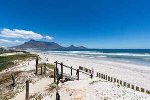 A beach with a wooden fence, sandy dunes, and a mountain in the background. - Lagoon Beach Penthouse (Cape Town)