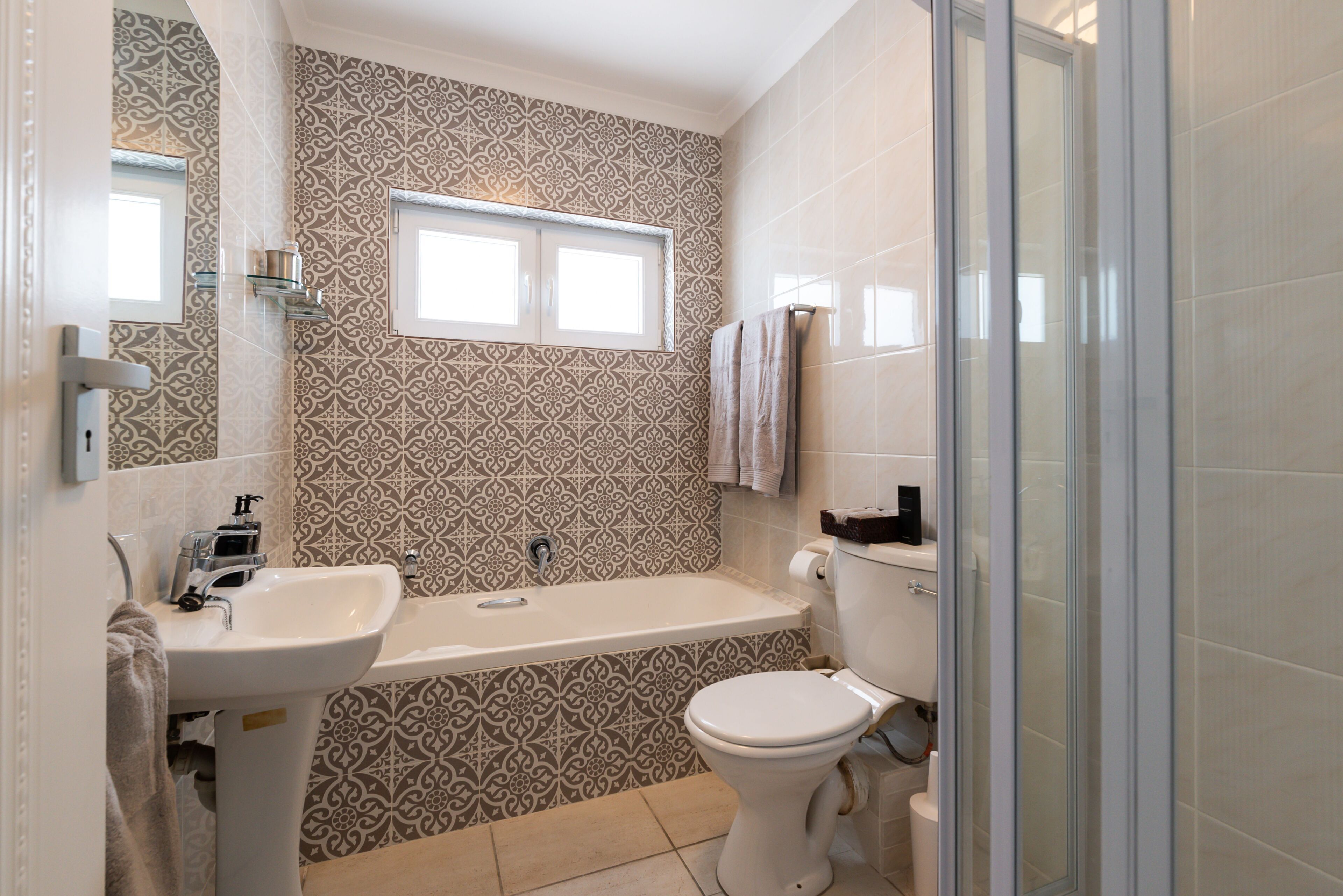 A bathroom with a patterned tile wall, a sink, a bathtub, and a toilet.