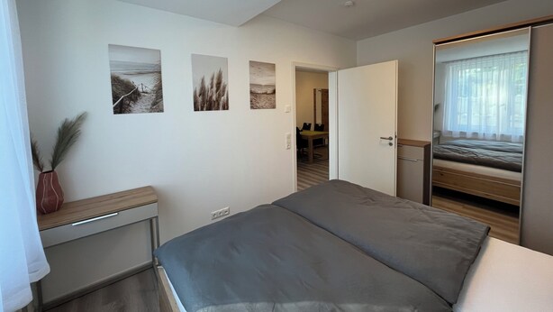 Ein Schlafzimmer mit einem Bett, einem Schreibtisch und einem Stuhl. An der Wand hängen drei Bilder in Rahmen.