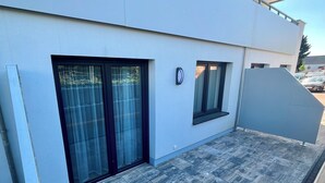 Ein modernes Gebäude mit flachem Dach, einer Schiebetür aus Glas, einem kleinen Fenster und einem Metallgeländer.
