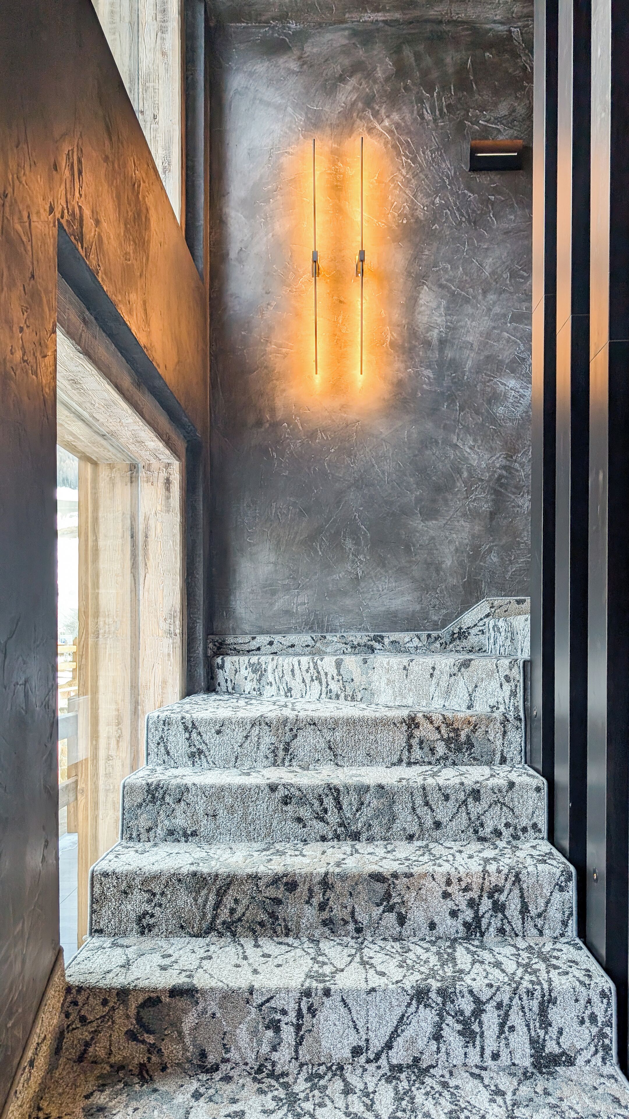A staircase with a marble finish, leading to a room with a textured wall and a light fixture.