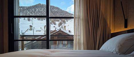 A hotel room with a large window offering a view of a snowy mountain landscape.